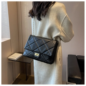 Detail of black quilted leather shoulder bag with gold chain strap and metal turn-lock