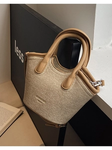 Minimalist beige canvas bucket bag with brown leather handles and adjustable shoulder strap