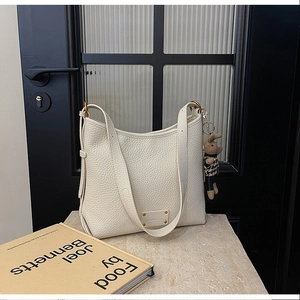 Close-up of white lychee pattern hobo bag with teddy bear charm on stone surface