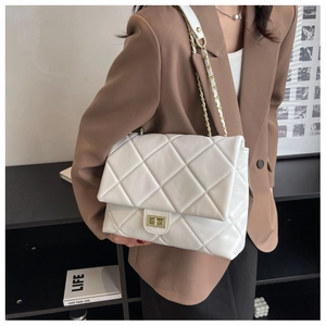 Detail of white quilted chain bag with gold turn-lock worn by a model in a brown blazer