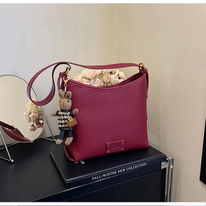 Detail of burgundy lychee leather bucket bag with cute rabbit charm and flower accent