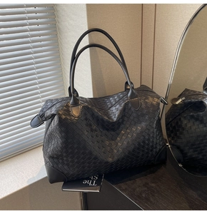 Close-up of the black woven tote bag showing the texture and leather corner reinforcement