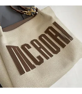 Detail of canvas tote featuring textured MCHANL lettering and brown leather shoulder strap