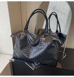 Detail of black woven leather tote bag featuring dual handles and secure zip closure