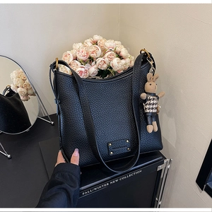 Detail of black lychee leather bucket bag featuring a gold ring and a small bunny pendant