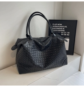 Detail of black woven leather tote bag showing Intrecciato craftsmanship on white podium