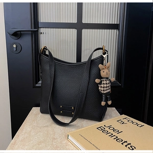 Close-up of black lychee grain leather bucket bag with a cute rabbit charm and gold plaque