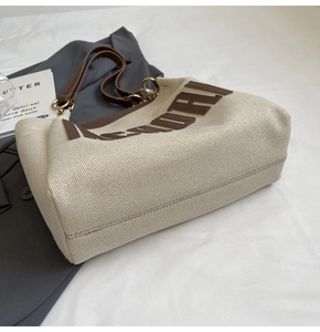 Detail of canvas tote bag showing brown leather handles and sturdy base stitching