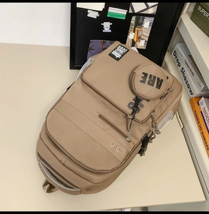 Close-up of khaki backpack with side mesh pockets and a round 'ARE' letter charm