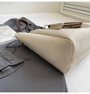 Detailed side view of canvas tote bag with brown leather H-pattern and stitching