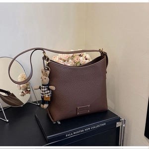 Detail of brown lychee leather bucket bag with gold logo and cute bunny charm pendant