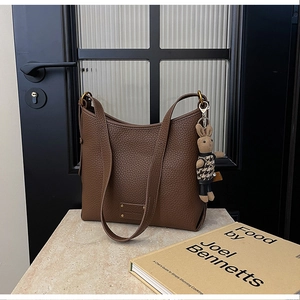 Detail of coffee brown lychee leather Hobo bag with plush rabbit charm and metal logo