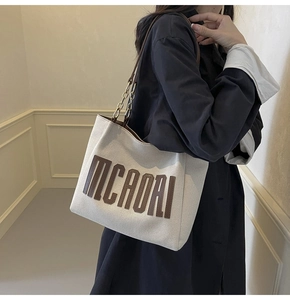 Detail of canvas tote bag featuring brown leather lettering and gold chain accents