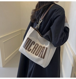 Detail of canvas tote bag featuring MCADAI leather patch and metal chain strap accent