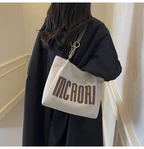 Detail view of large canvas tote bag with brown leather straps shown on model in black coat