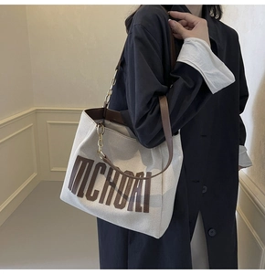 Detailed view of cream canvas tote bag with brown leather trim and metallic chain details