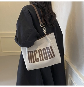 Detail of canvas tote bag with MCAORI logo, leather strap and metallic chain detail