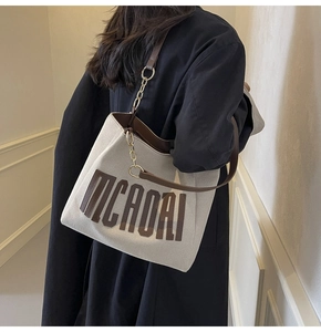 Detail of canvas tote bag with brown leather trim and metal chain strap worn by a model