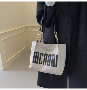 Detail of canvas tote bag featuring black MCAORI logo and gold chain shoulder strap