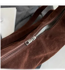Macro detail of dark brown suede shoulder bag featuring a smooth silver metal zipper