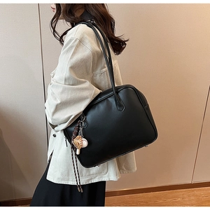 Détail d'un sac cabas en cuir noir avec pendentif baseball sur la bandoulière