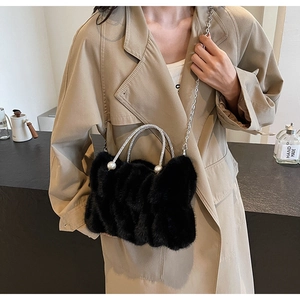 Detail van pluizige zwarte wolktas met strass handvat en parelketting op een trenchcoat