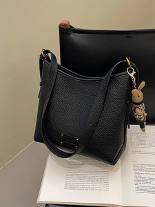 Modern black lychee grain leather bucket bag with a cute rabbit pendant on a book background