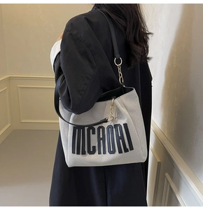 Detail of canvas tote bag with black leather straps and MCAORI logo and gold chain