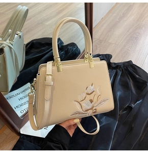 Close-up of floral embroidery on off-white handbag with gold hardware and top handle