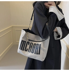Detailed view of beige tote bag with black MCAOAI lettering and chain shoulder strap