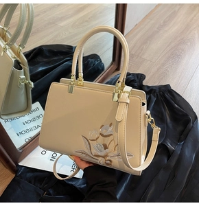 Detail of beige tote bag featuring elegant tulip embroidery and metallic gold buckles