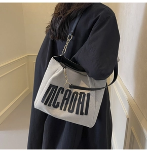 Close-up of large canvas tote bag with black MCAORI logo and gold chain leather strap