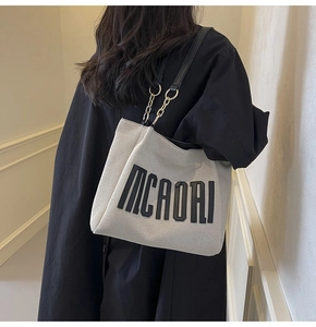 Detail of grey canvas tote bag with black leather chain strap and embossed logo
