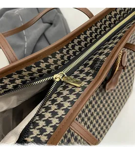Close-up of smooth gold metal zipper and houndstooth fabric texture on tote bag