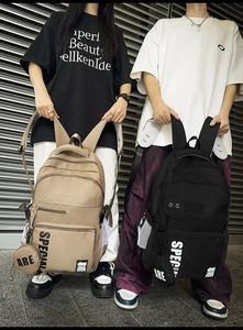 Detail of tan and black large nylon backpacks with multi-pocket design and bag charms