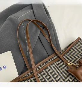 Detail of houndstooth tote bag with brown leather handles and a bear charm on a grey blazer