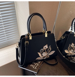 Detail of tulip embroidery and gold hardware on black structured leather tote bag