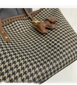 Detail of houndstooth fabric tote bag with brown leather handles and dog charm decor
