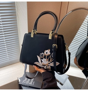 Detail of floral embroidery on a black leather handbag with elegant gold hardware