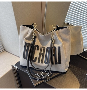 Detail view of large canvas tote bag with black leather handle and metal chain