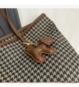 Detail of houndstooth fabric tote bag with brown leather trim and a dog-shaped charm