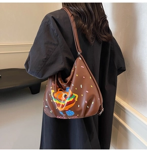Detail of a large brown leather tote featuring a cartoon burger and hello graphic
