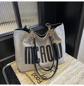 Detail of grey-white tote bag with black leather trim and elegant gold chain strap
