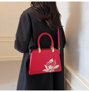 Detail view of red square handbag with elegant floral embroidery and golden hardware