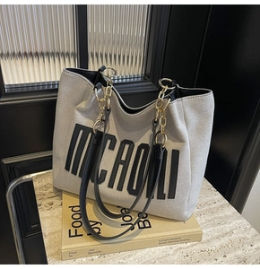 Detail of off-white canvas tote with black lettering and leather chain strap
