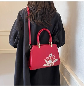 Detailed close-up of a red leather handbag with white floral embroidery and gold metal hardware