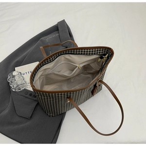 Detail view of large houndstooth tote bag featuring leather handles and zipper inner pocket