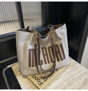 Detail of canvas tote bag with letter patch and gold chain strap on marble surface