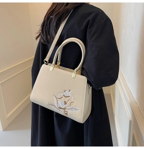 Detailed view of cream handbag with floral embroidery and gold metal hardware on model