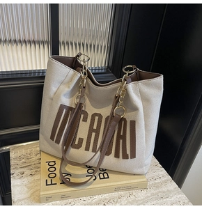 Detail of canvas tote bag showing MICAI logo, leather piping, and metal chain handle